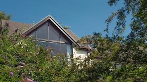 A modern house with large windows and a sloped roof, surrounded by lush greenery. - Rhyd y Groes, Holiday Cottage Burton, Sleeps 10, 5 bedrooms,  bathrooms (Milford Haven)