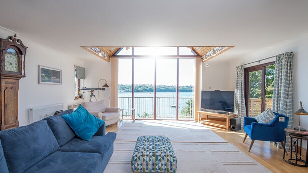 A spacious living room with a large sofa, ottoman, and a television. There is a balcony with a view of the water and a wooden ceiling. - Rhyd y Groes, Holiday Cottage Burton, Sleeps 10, 5 bedrooms,  bathrooms (Milford Haven)