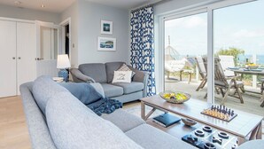 A modern living room with a grey sofa, a coffee table with chess and board games, and a view of the sea through large windows. - Robin Hill, Holiday Cottage Tresaith, Sleeps 5, 3 bedrooms,  bathrooms (Cardigan)