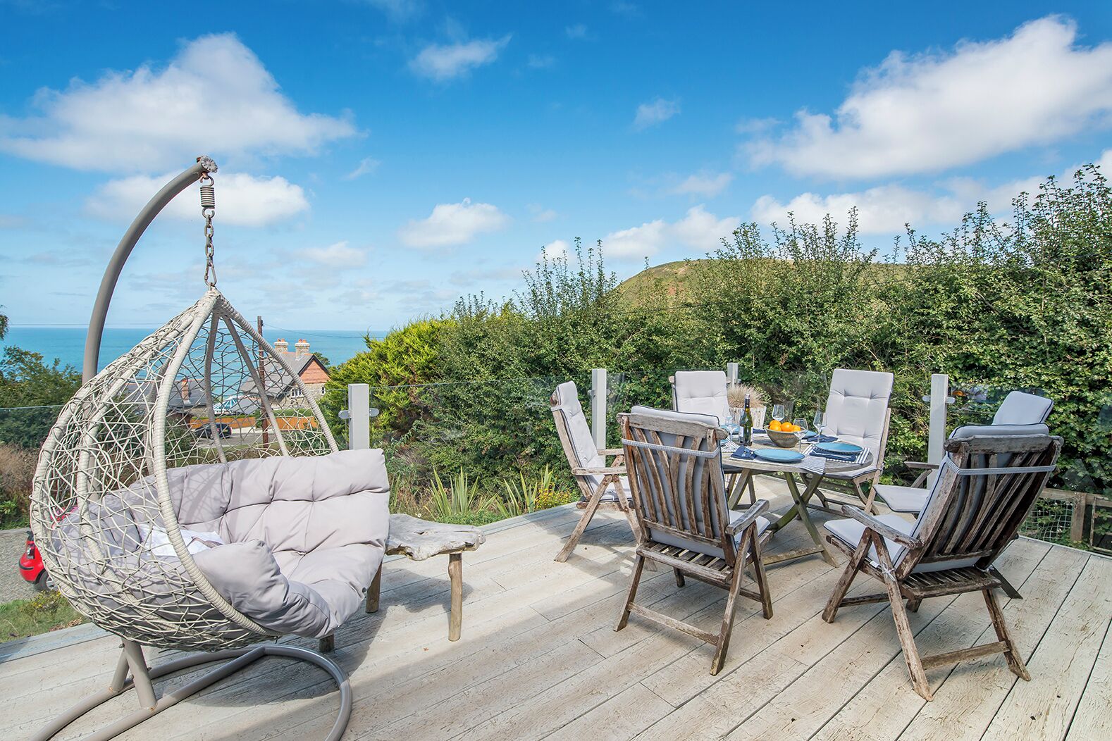 A wooden deck with a hanging chair, a table set for dining, and chairs.