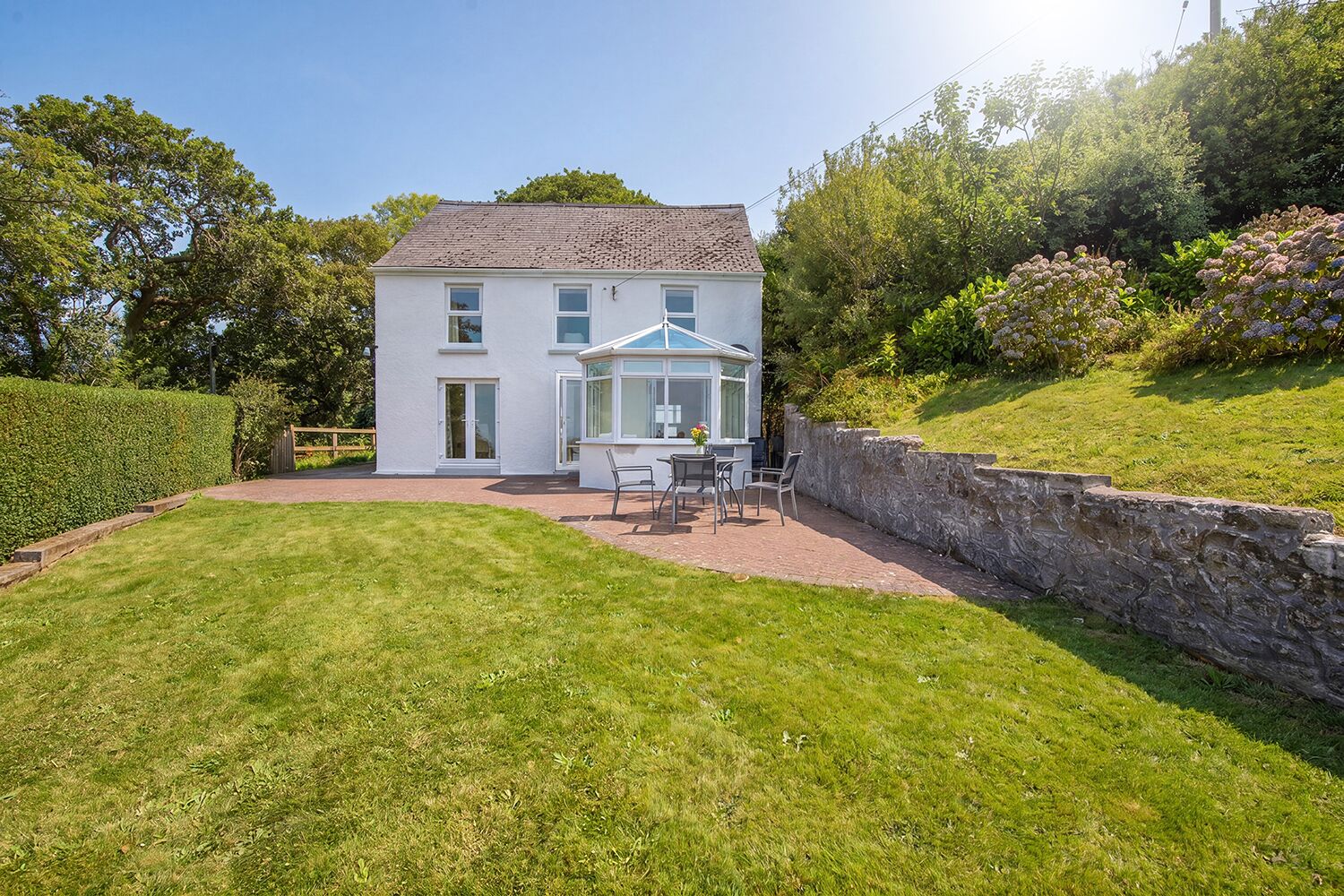 A two-story house with a conservatory, a paved patio, and a stone wall.
