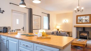 A modern kitchen with a wooden countertop, white cabinets, and a dining area with a sofa and a fireplace. - Salar, Holiday Cottage Lawrenny, Sleeps 4, 2 bedrooms,  bathrooms (Lawrenny)