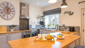 A modern kitchen with a wooden island, stainless steel appliances, and a large wall clock. - Salar, Holiday Cottage Lawrenny, Sleeps 4, 2 bedrooms,  bathrooms (Lawrenny)