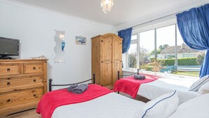 A bedroom with two beds, wooden wardrobe, TV, and a window with curtains. - Sandgrove, Holiday Home Saundersfoot, Sleeps 4, 2 bedrooms,  bathrooms (Saundersfoot)