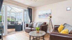 A spacious living room with a large glass door leading to a balcony, a round coffee table, and two sofas with cushions. - Sandgrove, Holiday Home Saundersfoot, Sleeps 4, 2 bedrooms,  bathrooms (Saundersfoot)