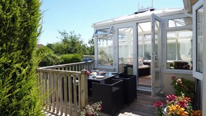 A conservatory with a wooden deck, a table with chairs, and a view of the garden. - Sandgrove, Holiday Home Saundersfoot, Sleeps 4, 2 bedrooms,  bathrooms (Saundersfoot)