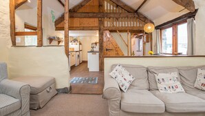 A cozy living room with a sofa, a chair, and a staircase leading to a kitchen. - Seahorse Cottage, Holiday Cottage Aberfforest Beach, Newport, Sleeps 6, 3 bedrooms,  bathrooms (Newport)
