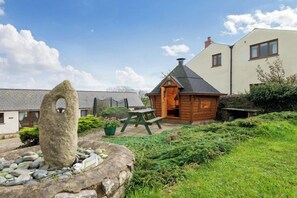 Eine rustikale Holzhütte mit einem Steinfeuerwerk, einem Picknicktisch und einem kleinen Gartenbereich.