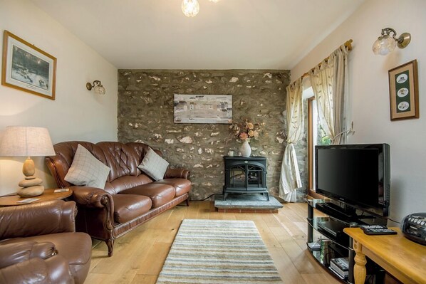 Ein gemütliches Wohnzimmer mit braunem Ledersofa, einer Steinwand, einem Kamin, einem Fernseher und einem Holztisch.