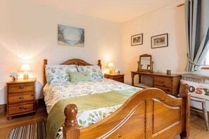 Ein Schlafzimmer mit einem Holzbett, zwei Nachttischen mit Lampen, einer Kommode, einem Spiegel und einem Sessel.