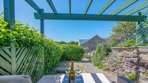 A table with a bottle and glasses, a stone wall, and a wooden fence in a garden setting. - Silk Purse, Holiday Home Angle, Sleeps 4, 2 bedrooms,  bathrooms (Angle)