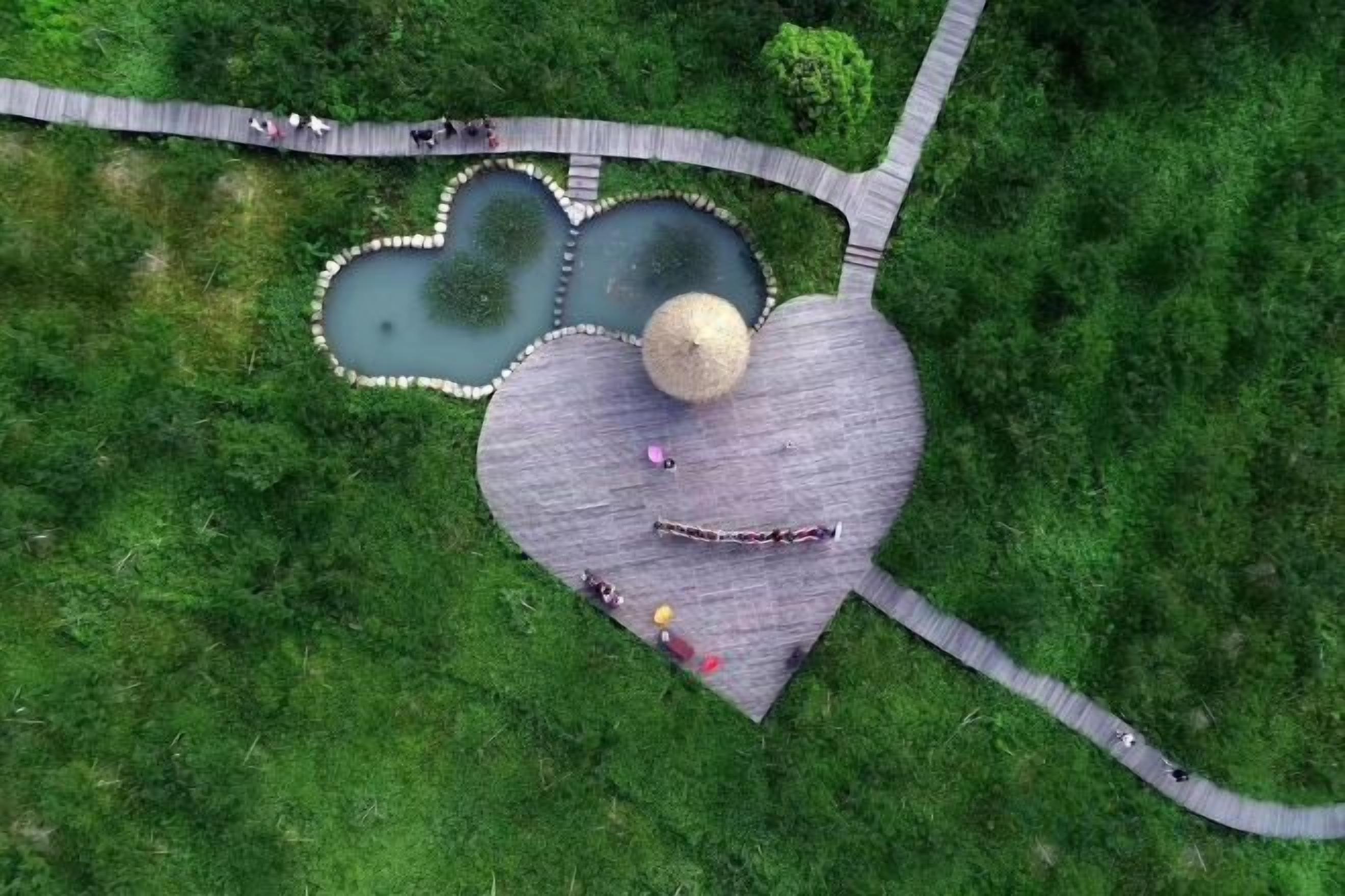 An aerial view of a park with a heart-shaped structure, a pond, and a walking path.