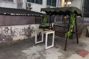 A patio area with a table and bench under a green umbrella, a concrete floor, and a wall with peeling paint. - MiaoJu (Yueqing)