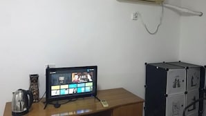 A room with a wooden desk, a television, a kettle, a small cabinet, and an air conditioner on the wall. - MiaoJu (Yueqing)
