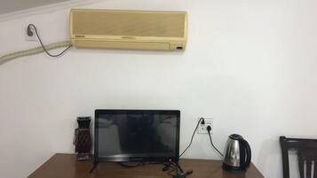 A room with a wooden table, a black monitor, a kettle, and a wall-mounted air conditioner.