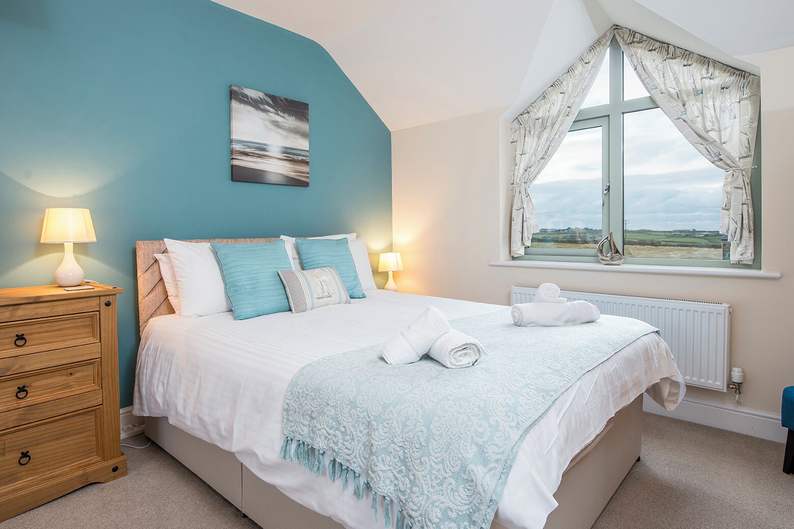 A bedroom with a bed, a nightstand, a window with curtains, and a view of the countryside.
