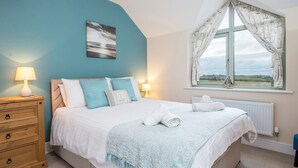 Un dormitorio con cama, mesita de noche, ventana con cortinas y vistas al campo.