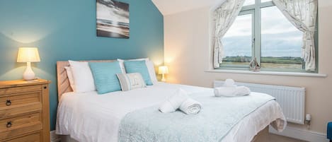 A bedroom with a bed, a nightstand, a window with curtains, and a view of the countryside.