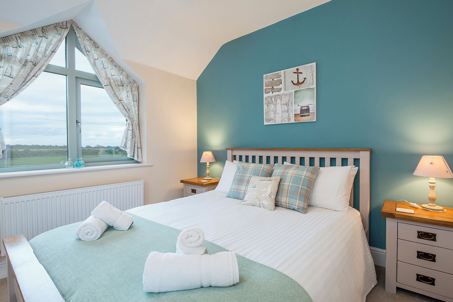 Un lit bien fait, avec du linge de lit blanc et des touches de bleu, une fenêtre avec des rideaux et un mur décoré sur le thème de la marine.
