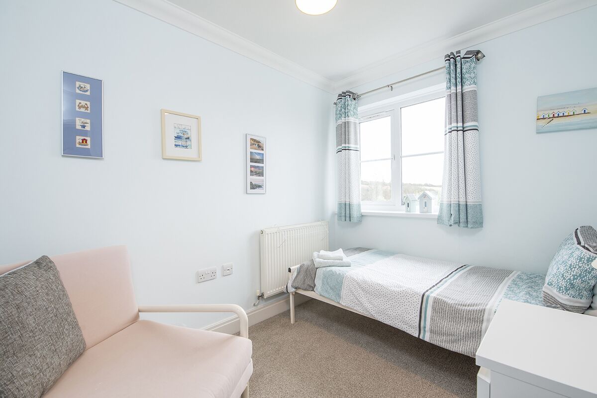 A bedroom with a single bed, a bedside table, a chair, and a window with curtains.
