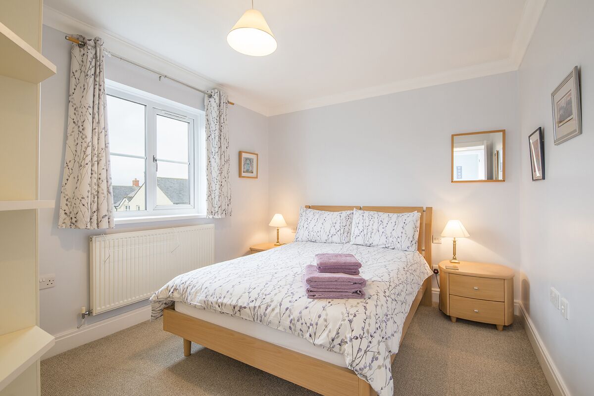 A bedroom with a bed, two bedside tables, a window with curtains, a radiator, and a view of buildings outside.