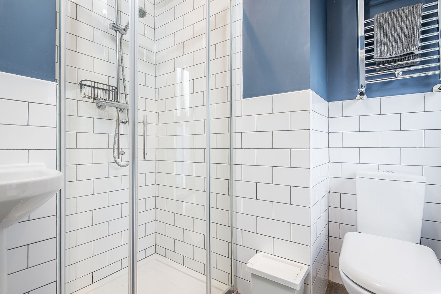 Ein Badezimmer mit einer Duschkabine, weißen Fliesen, einem weißen Waschbecken und einer Toilette.