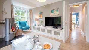 A living room with a fireplace, a TV, a blue armchair, and a dining area with a table set for two.