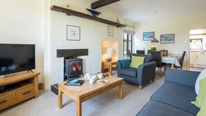 A cozy living room with a fireplace, a television, and a dining area with a table and chairs. - Sunnybank, holiday property Manorbier, Sleeps 6, 3 bedrooms,  bathrooms (Manorbier)