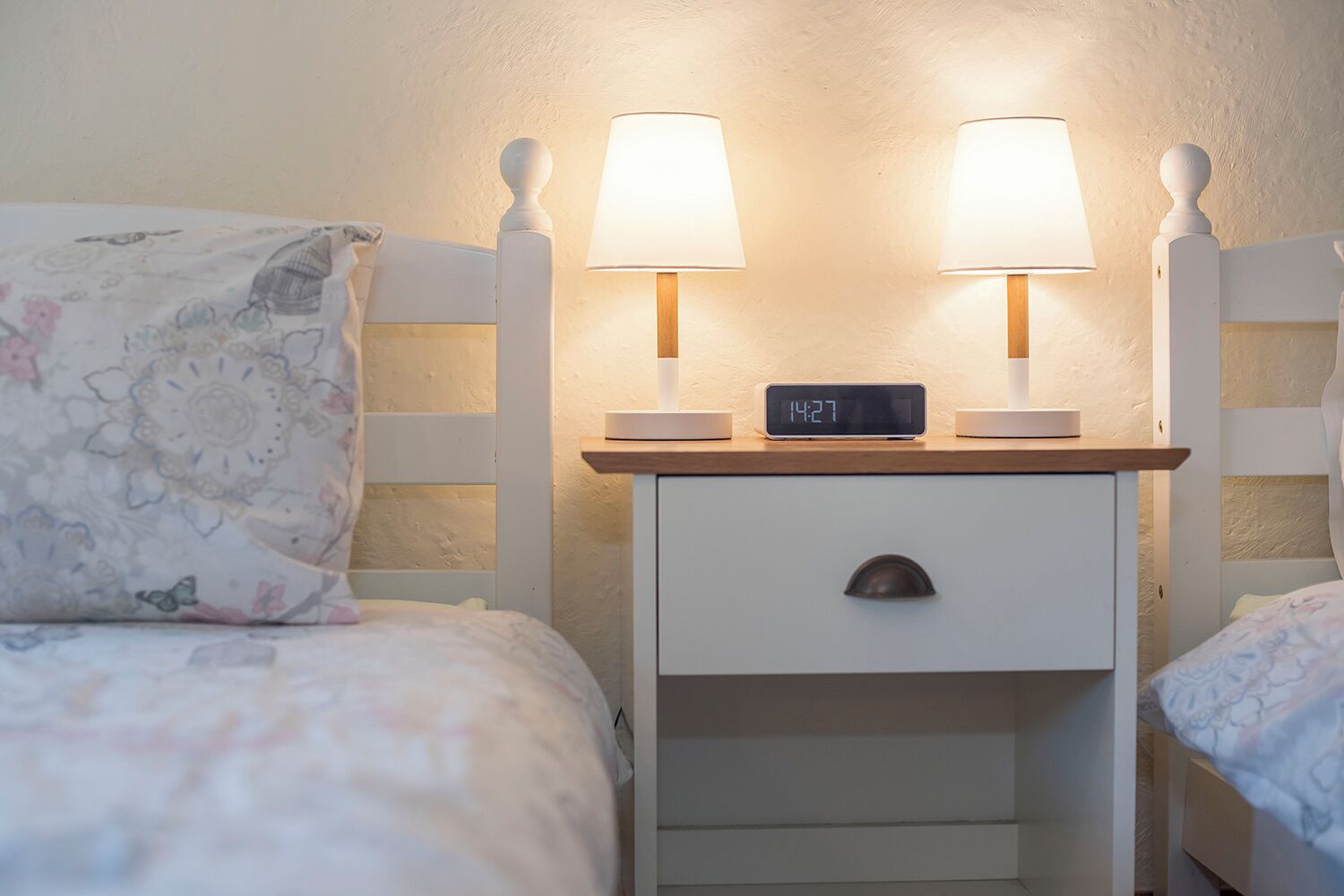 A bedroom with two beds, each with a nightstand, a lamp, and a digital clock.