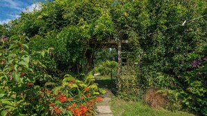 A garden pathway with a wooden archway surrounded by lush greenery and flowering plants. - Sunnybank, holiday property Manorbier, Sleeps 6, 3 bedrooms,  bathrooms (Manorbier)