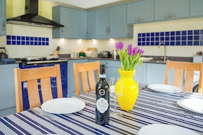 A dining table with a bottle of wine, a yellow vase with flowers, and a striped tablecloth.