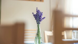 Une table sur laquelle est posé un vase en verre transparent contenant des fleurs de lavande, le tout sur une table recouverte d’une nappe blanche.