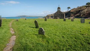 A grassy cemetery with stone headstones and a small stone building with a bell tower. - Swn y Mor, Holiday Apartment Pwllgwaelod, Sleeps 4, 2 bedrooms,  bathrooms (Dinas)