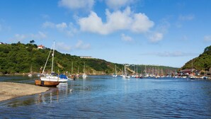 A harbor with boats docked along the shore, a building on a hill, and a clear blue sky. - Swn y Mor, Holiday Apartment Pwllgwaelod, Sleeps 4, 2 bedrooms,  bathrooms (Dinas)
