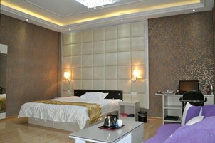 A hotel room with a large bed, bedside tables, a desk, and a purple sofa.