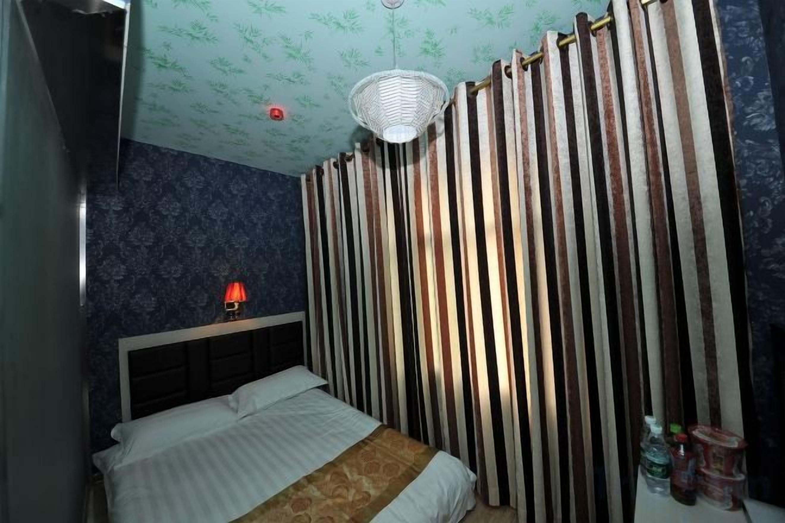 A bedroom with a bed, a nightstand, a lamp, and a curtain.