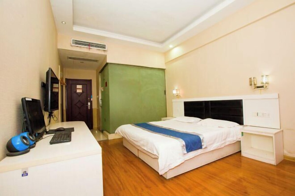 A hotel room with a bed, bedside tables, a desk with a computer, and a TV.