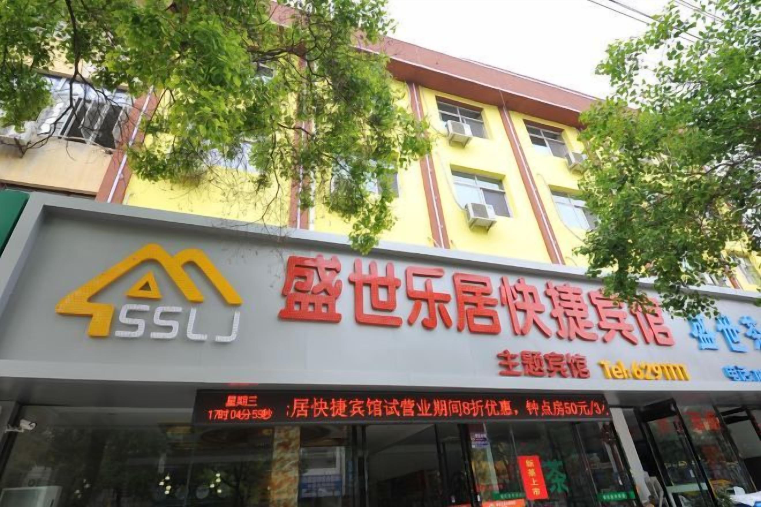 A hotel with a yellow facade and a signboard displaying the name and contact information.