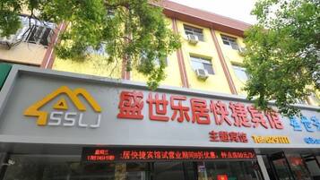 A hotel with a yellow facade and a signboard displaying the name and contact information.