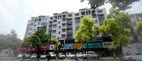 Un edificio de varios pisos con locales comerciales en la planta baja, coches estacionados y árboles en la parte delantera.