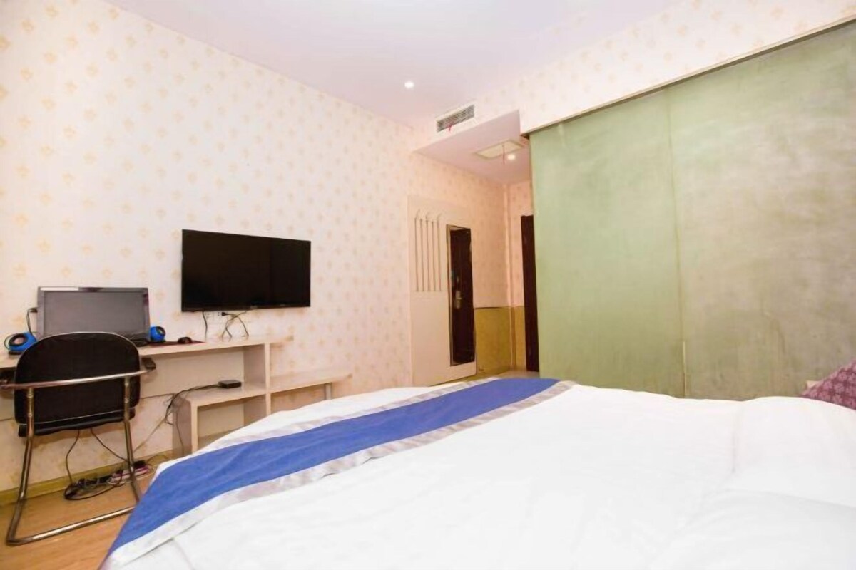 A hotel room with a bed, a desk with a computer and speakers, a TV, and a wardrobe.