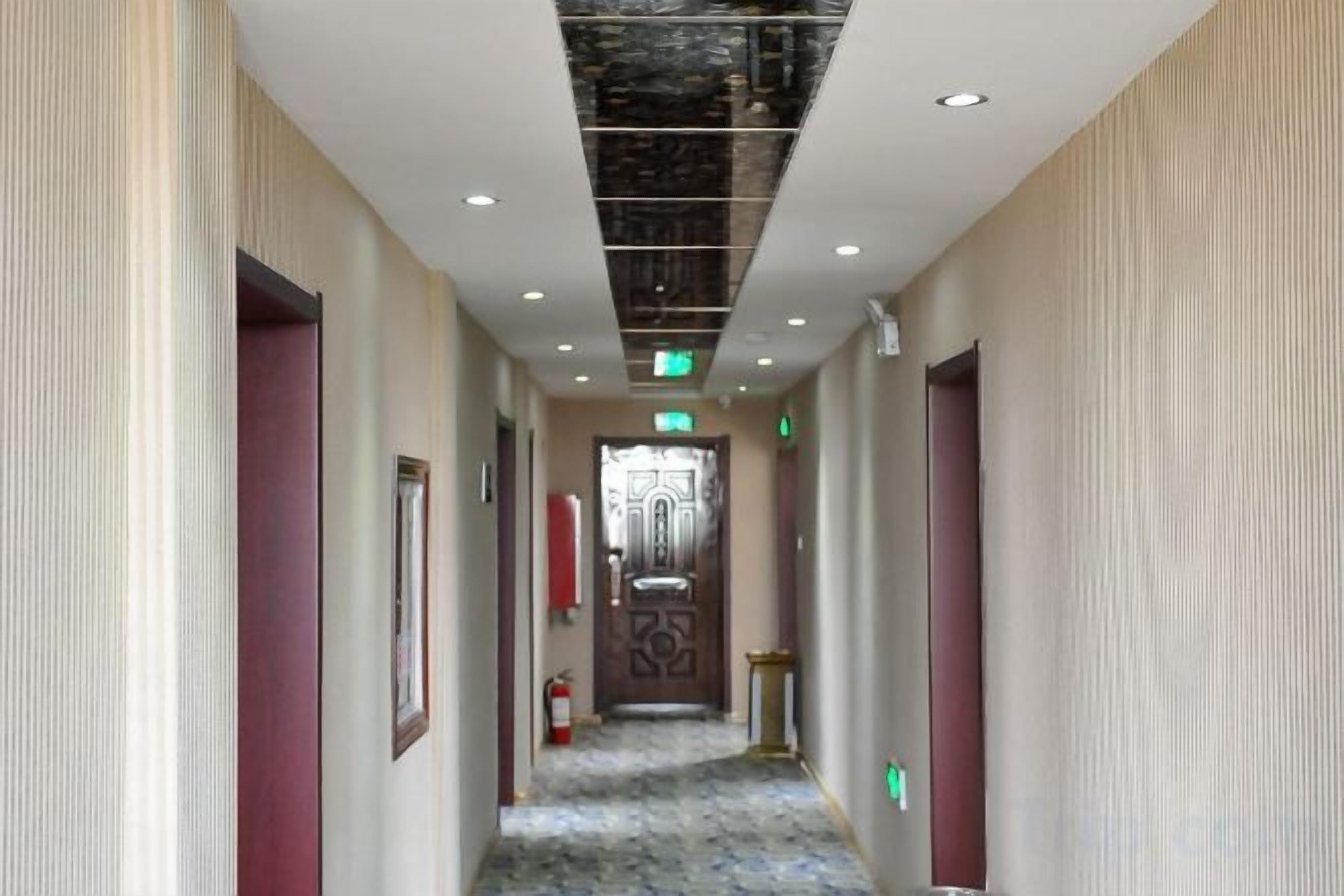 Un pasillo de hotel con puertas a ambos lados, suelo estampado e iluminación empotrada en el techo.