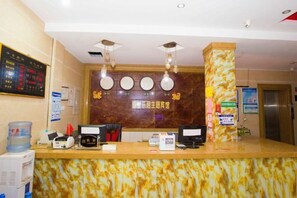Un comptoir d’accueil d’hôtel avec un revêtement en marbre, deux postes de travail pour les réceptionnistes, un distributeur d’eau et un panneau d’affichage numérique.