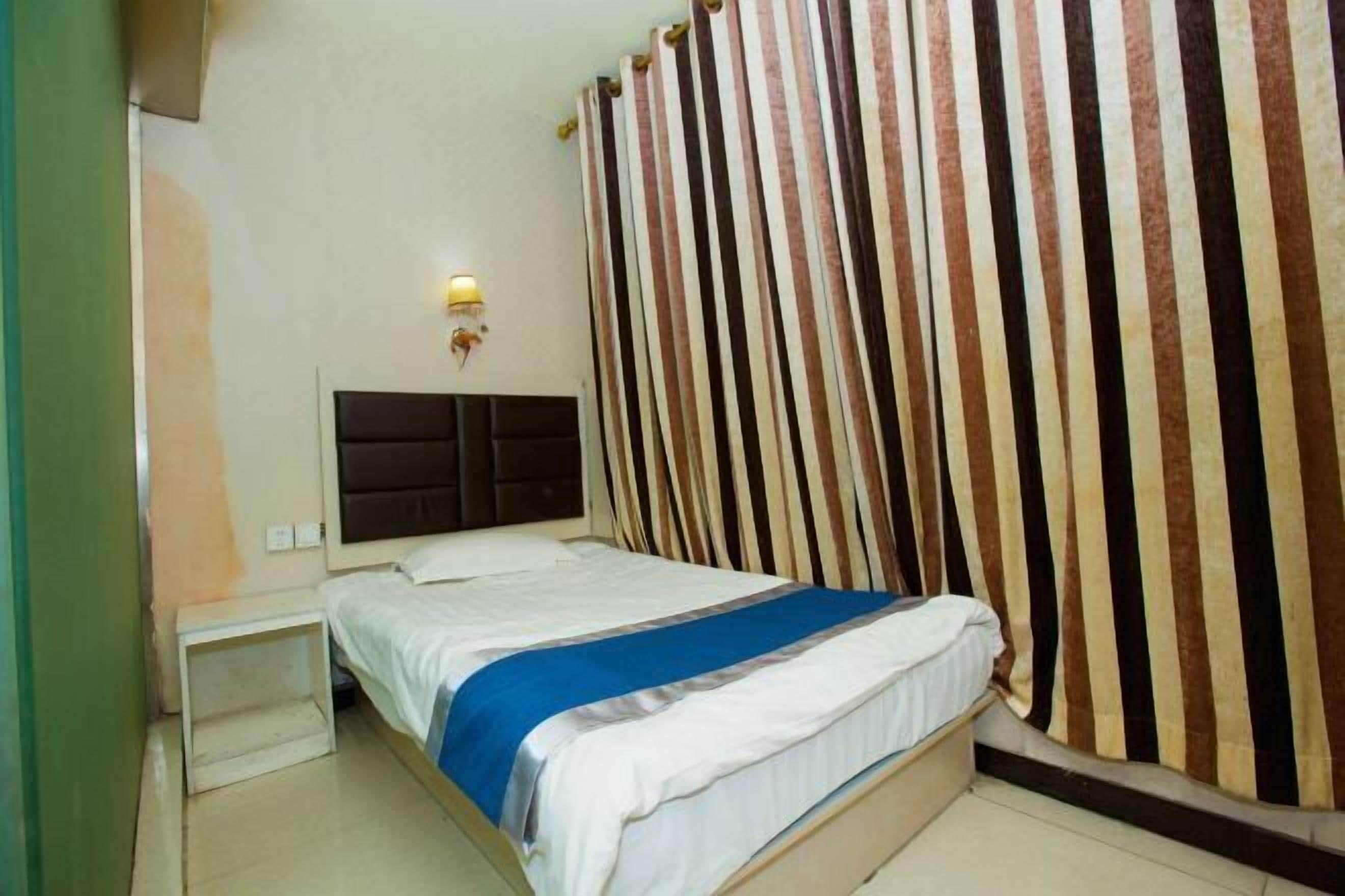 Una habitación de hotel con cama, mesita de noche, lámpara de pared y cortinas a rayas.