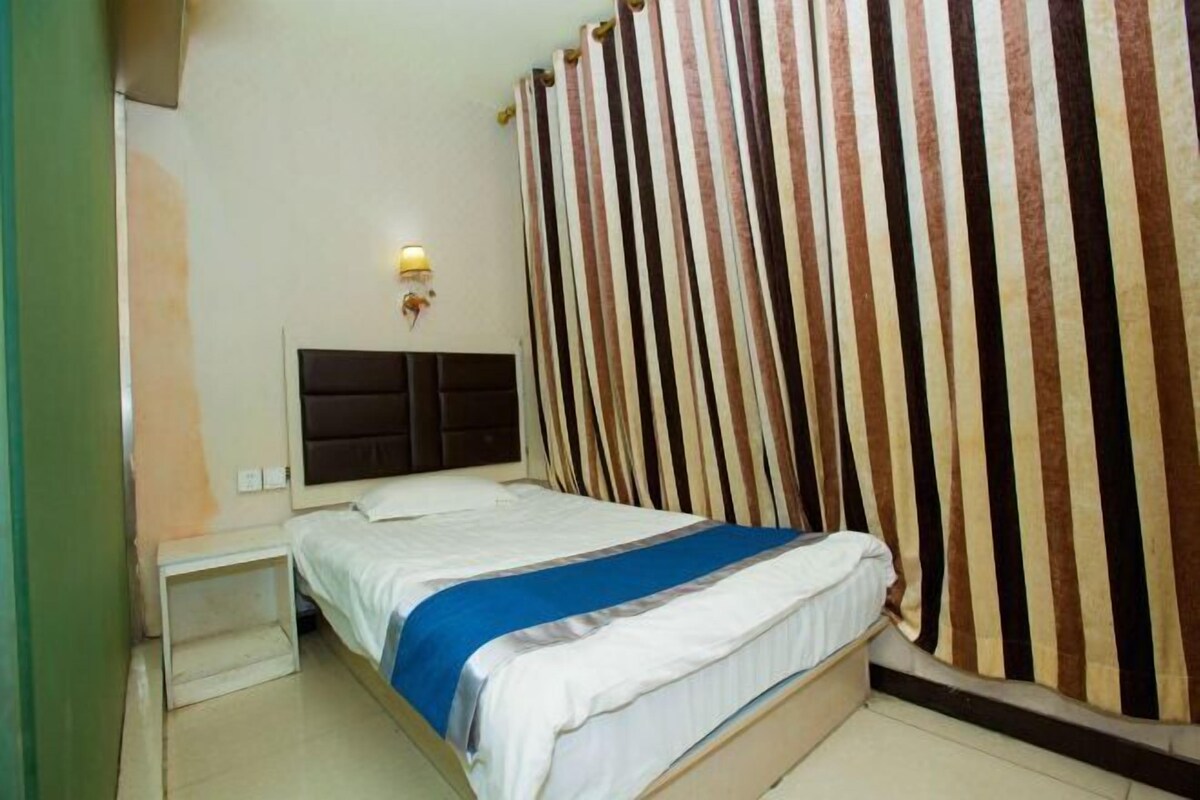 A hotel room with a bed, a nightstand, a wall-mounted light, and striped curtains.