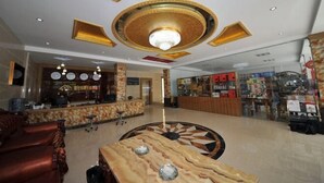 Un hall d’entrée spacieux avec une grande table ronde au centre, un comptoir d’accueil et, au fond, une variété de boutiques.