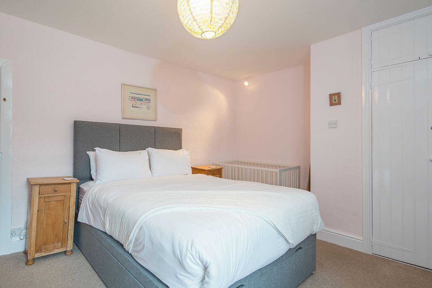 Une chambre à coucher comprenant un lit, une table de chevet, une commode, un radiateur et une porte.