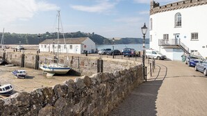 A coastal town with a stone wall, a white building with a balcony, and boats docked near the shore.