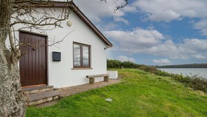 Un bâtiment blanc avec une porte et une fenêtre marron, un banc et des marches menant à la porte.