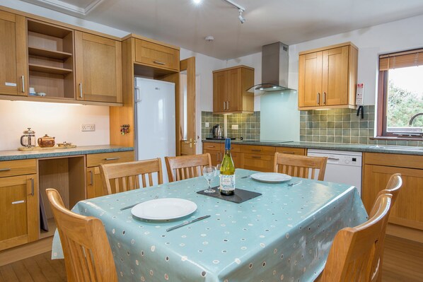 A kitchen with wooden cabinets, a dining table with a blue tablecloth, and a bottle of wine on the table.